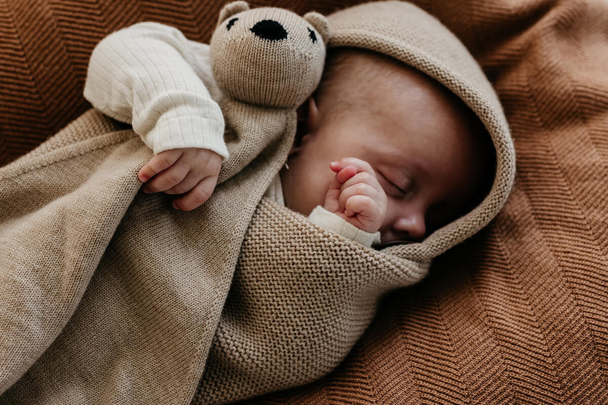 Niedliches Baby im gemütlichen Pucksack hält Kuscheltier im Arm - Geschenkidee für das erste Weihnachten