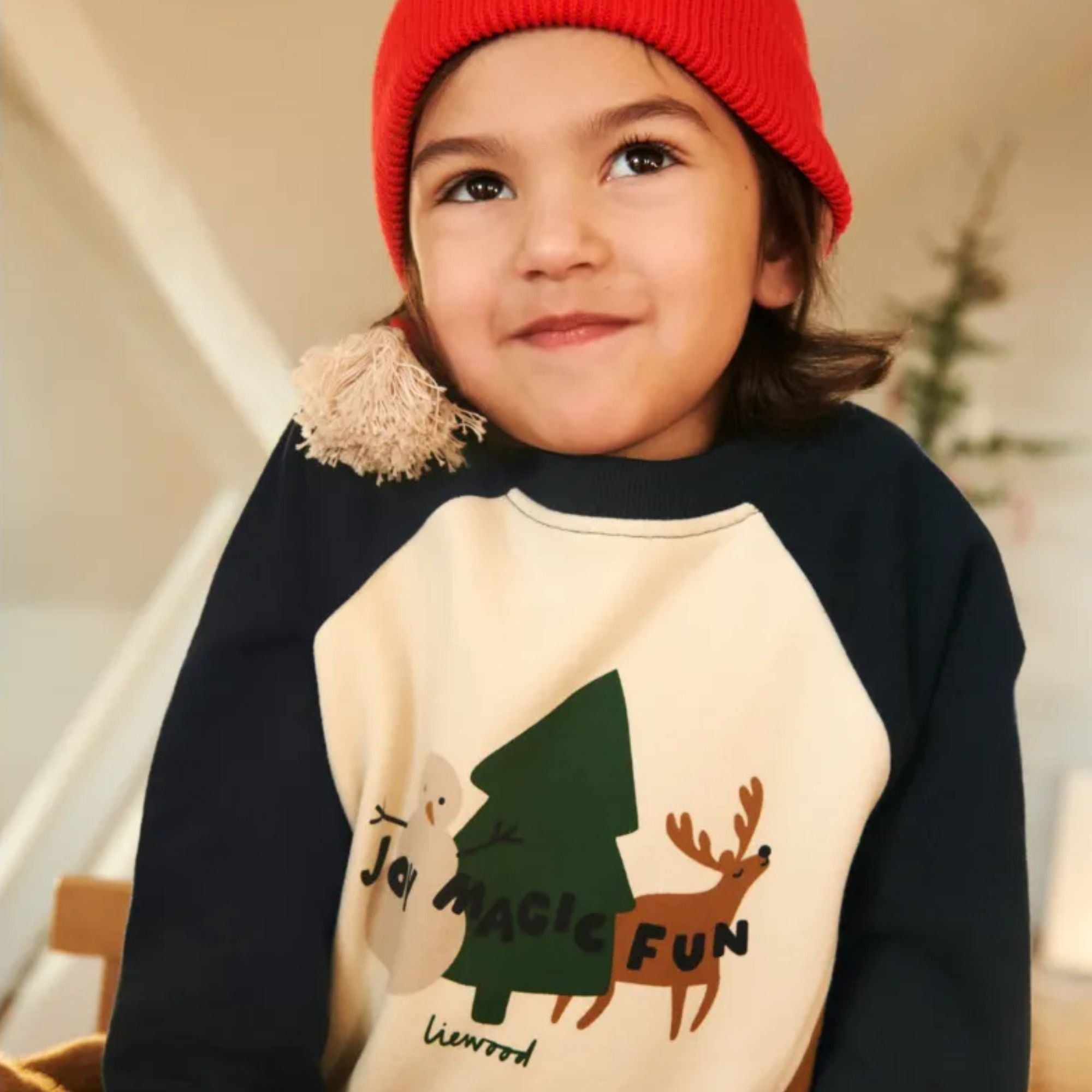 Kind mit roter Mütze trägt ein LIEWOOD-Sweatshirt mit Weihnachtsmotiv (Tannenbaum und Rentier) – Black Friday Aktion bei LibertyKids