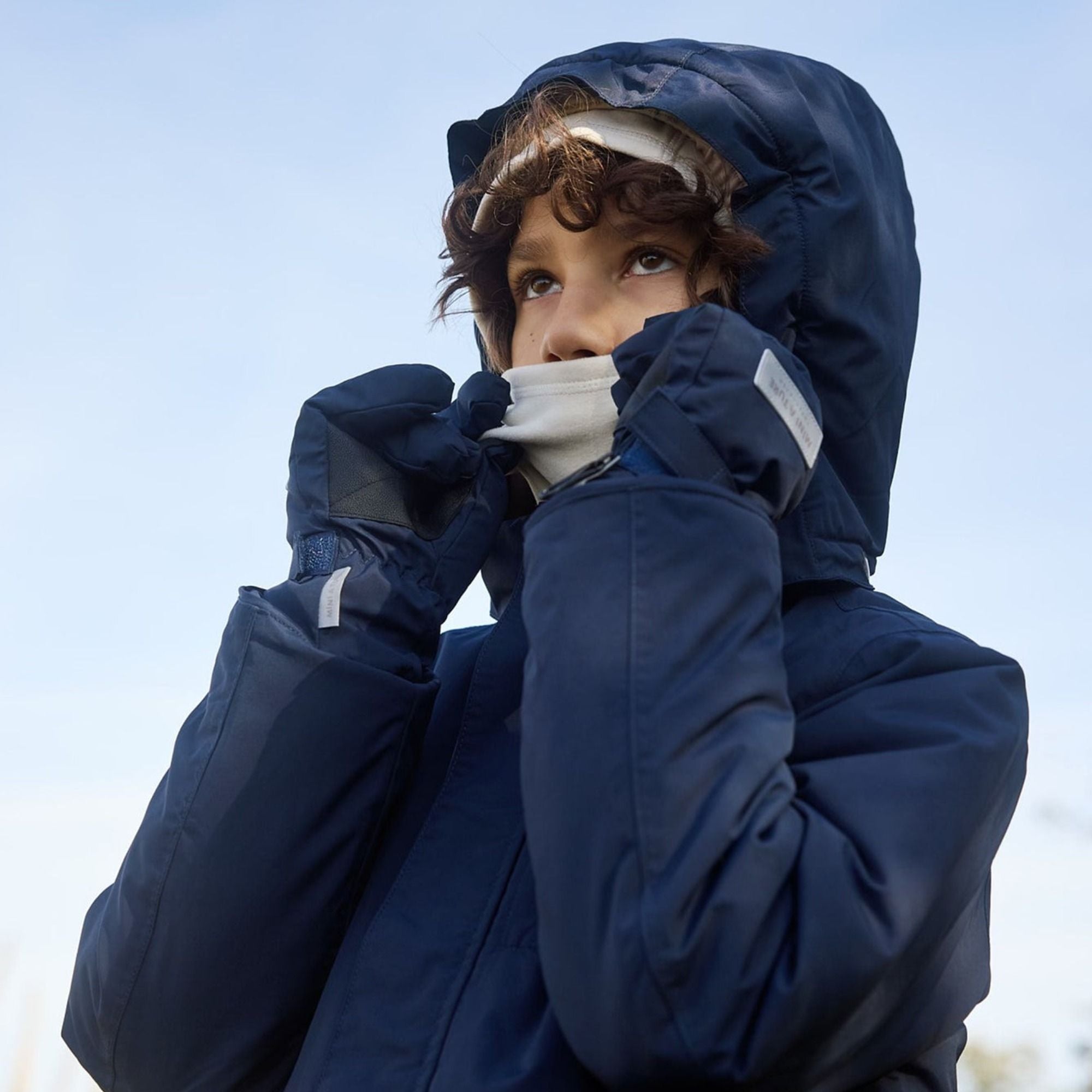 Junge mit dunkelblauer Winterjacke, Handschuhen und Mütze – passende Winteraccessoires für Kinder.