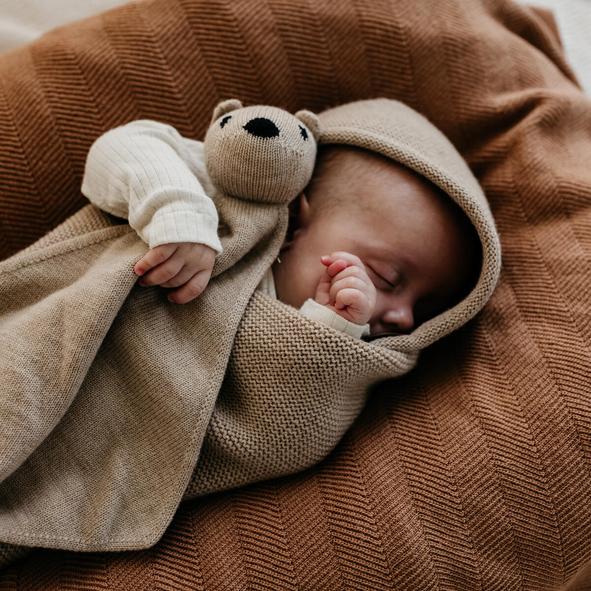 Niedliches Baby im gemütlichen Pucksack hält Kuscheltier im Arm - Geschenkidee für das erste Weihnachten