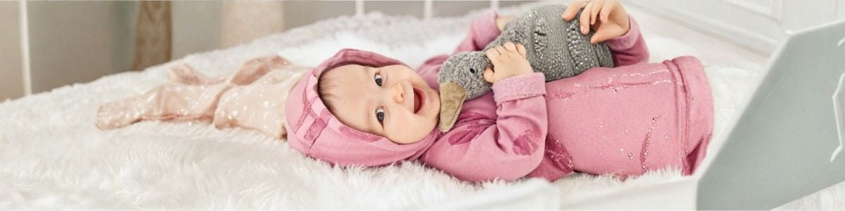 Lächelndes Baby in rosa Kleidung mit Kuscheltier – nachhaltige Babyprodukte bei LibertyKids