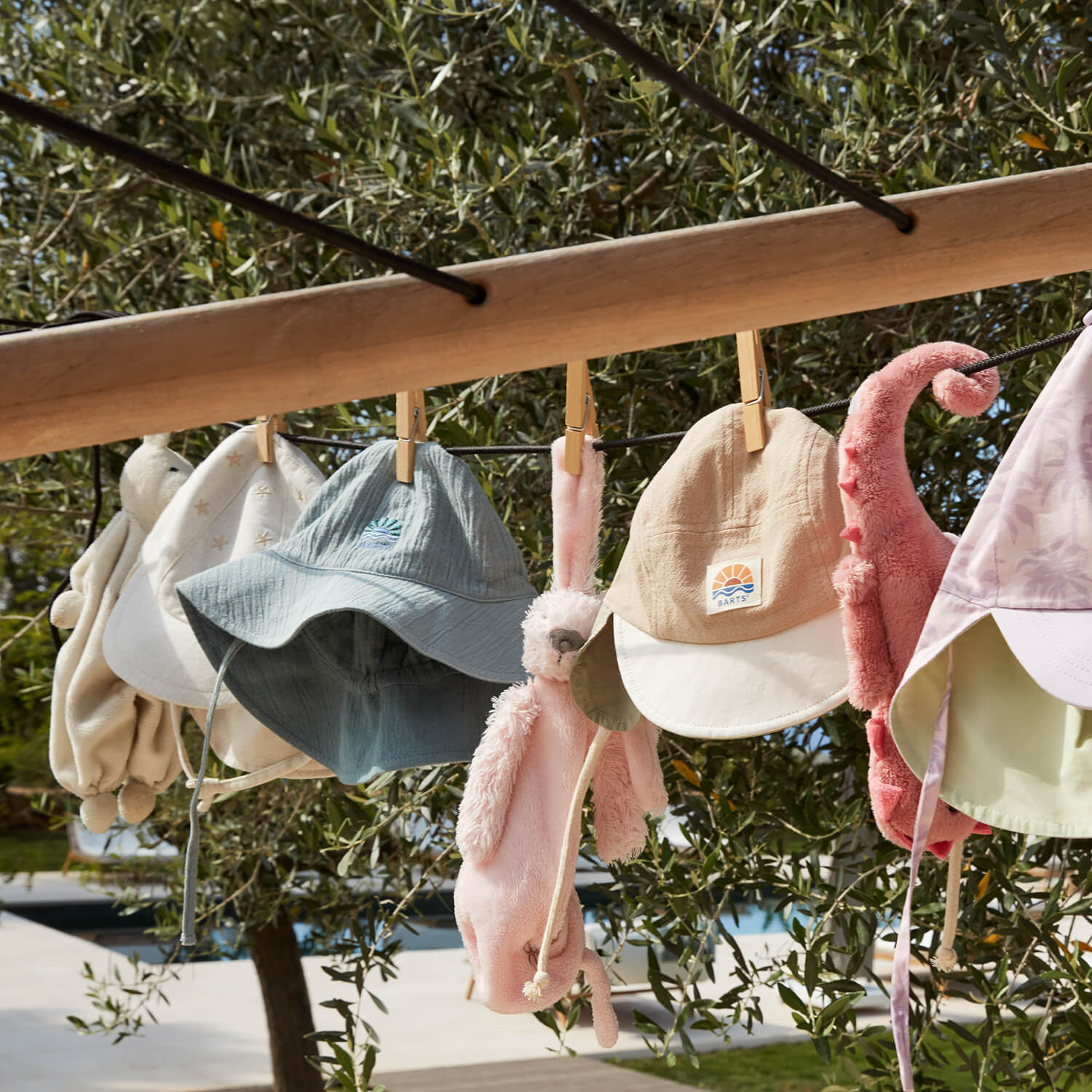 Verschiedene Mützen in sanften Farben hängen auf einer Holzstange im Freien – Barts Accessoires für Kinder