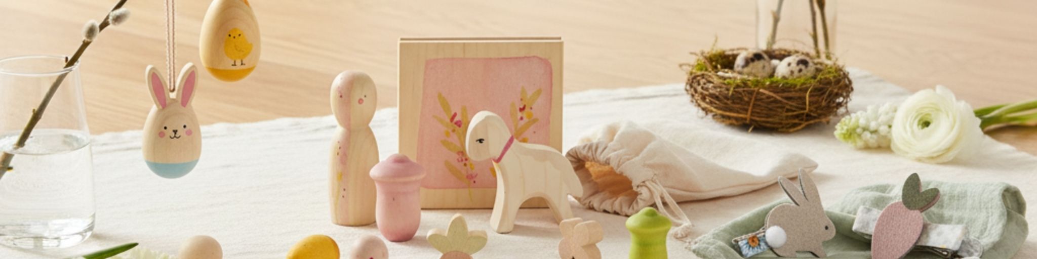 Besondere Ostergeschenke für Kinder und Babys, liebevoll arrangiert auf hellem Holz: Holz-Anhänger für den Osterstrauß, ein "Hello Spring" Holz-Spielset und süße Haarspangen-Sets. Nachhaltige und hochwertige Geschenkideen für das Osternest.