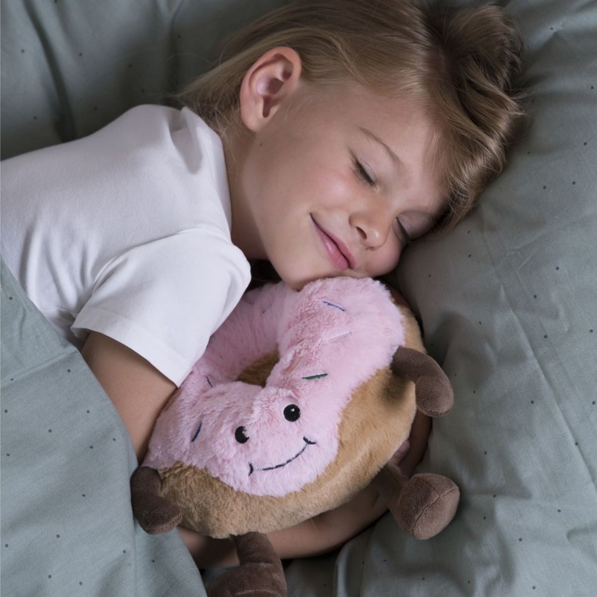 Kind kuschelt sich im Bett mit einem Warmies Donut-Wärmestofftier – mit Hirse-Lavendel-Füllung