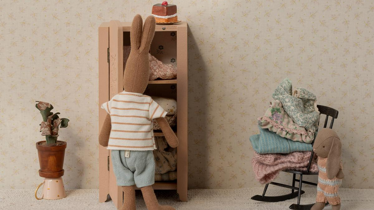 Ein Maileg Kleiderschrank aus Holz mit Miniatur-Kleiderbügeln und verschiedenen Stoff-Outfits für Mäuse und Hasen.