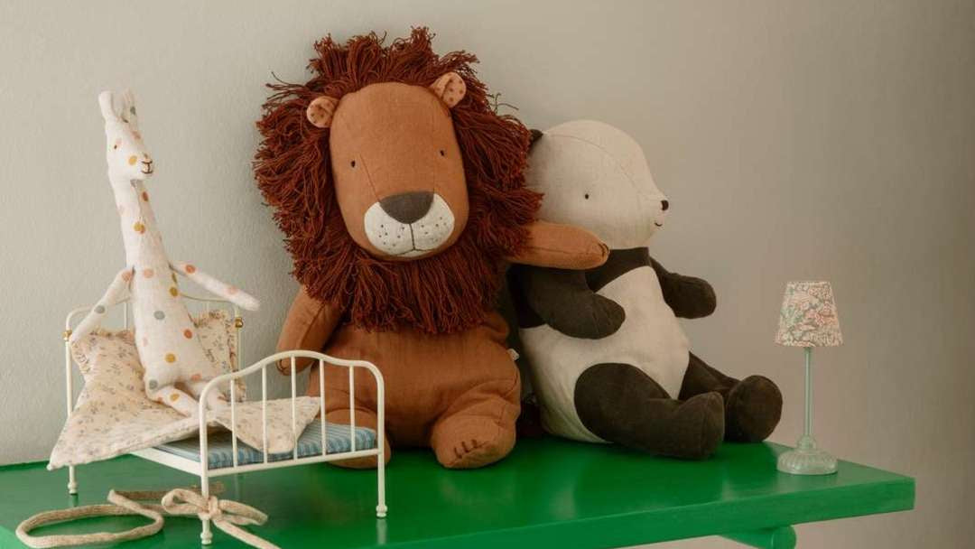 Maileg Kuscheltiere wie Löwe, Panda und Giraffe auf einem grünen Wandregal mit Stoff-Girlande im Kinderzimmer.