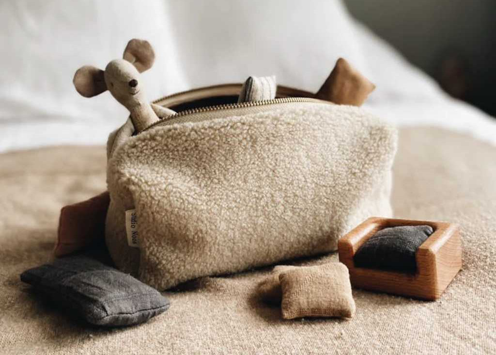 Eine Studio Noos Teddy Pouch in Ecru, gefüllt mit kleinen Spielsachen wie einer Stoffmaus, auf einem gemütlichen Bett.