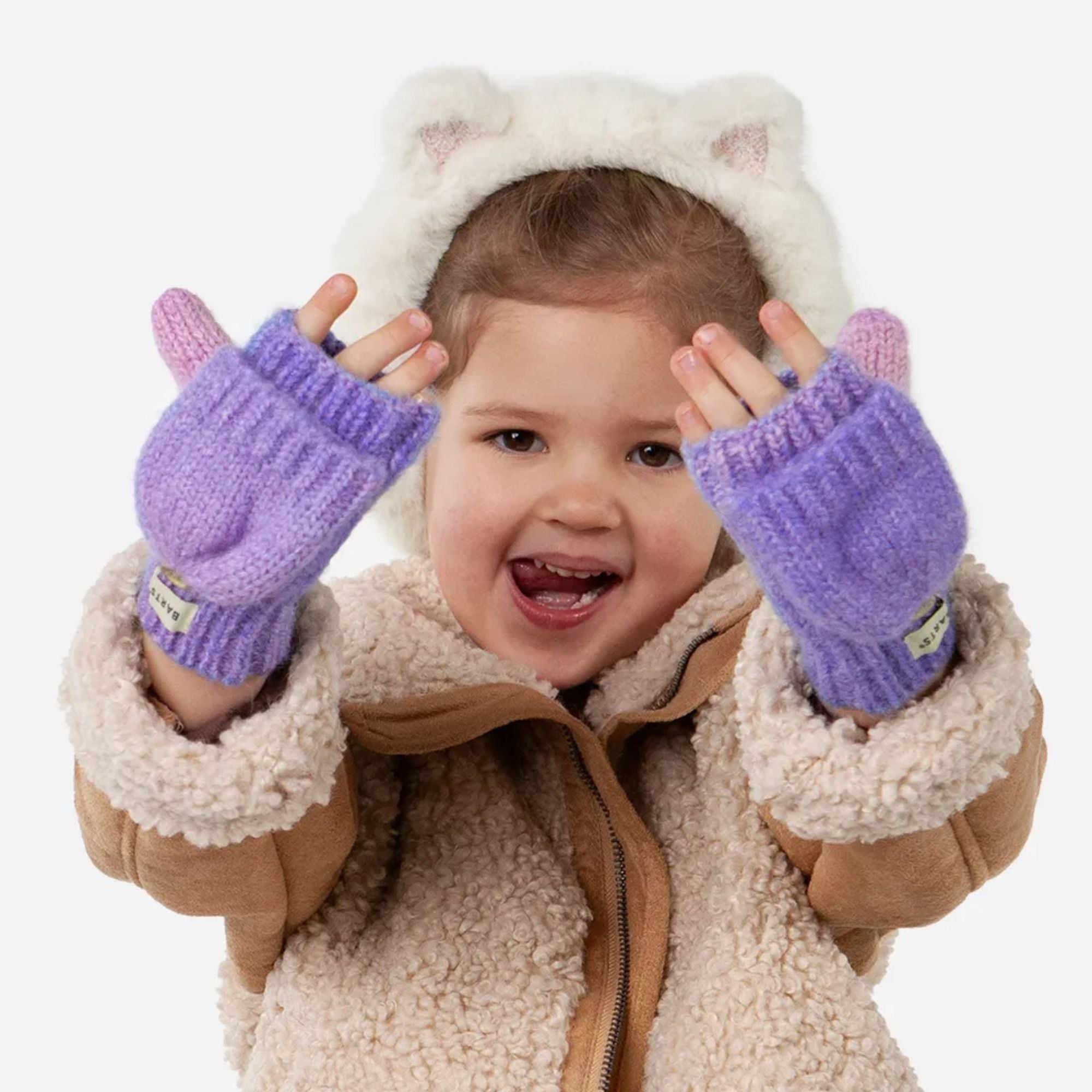 Kleinkind in warmer Winterkleidung mit flauschiger Bärchenmütze und lilafarbenen Handschuhen – fröhlich lachend.